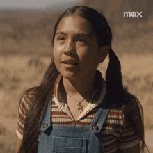 a young girl wearing overalls and a necklace with the word max on the bottom left