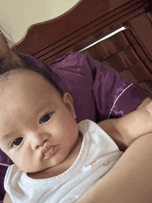 a baby in a white tank top is laying on a bed