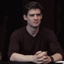 a young man is sitting at a table with his hand on his face and a watch on his wrist .
