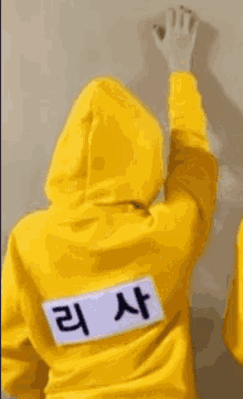 a child wearing a yellow hoodie is standing in front of a white wall .