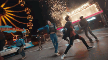 a group of people are dancing in front of a ferris wheel that says " don race "