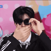 a man wearing sunglasses covering his mouth with his hands