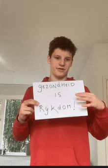 a young man in a red shirt holds up a sign that says gezondheid is rykdom