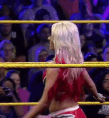 a woman in a red top and shorts is standing in a wrestling ring in front of a crowd .