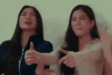 two women are giving each other a thumbs up and pointing at each other .