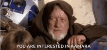 a man with a beard is sitting next to a robot and says `` you are interested in kamara ''