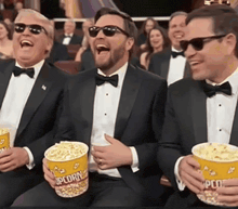 a group of men in tuxedos are laughing while holding buckets of popcorn