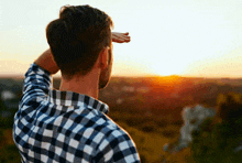 a man in a plaid shirt is looking out at the sunset .