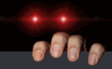 a close up of a person 's hands reaching out from behind a table with red lights behind them .