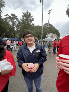 a man wearing an ole miss jacket holds a red cup in his hand