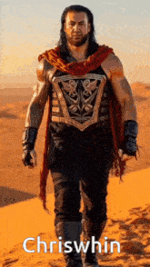 roman reigns is walking in the desert wearing a red scarf and a shield .