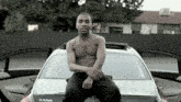 a shirtless man sits on the hood of a mercedes 5550