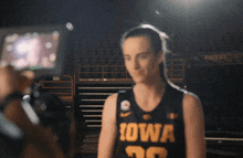 a woman in a iowa jersey stands in front of a sign that says hawks west
