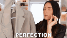 a woman adjusts her earring while holding a jacket with perfection written on it
