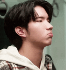 a young man wearing a plaid shirt and a white hoodie is making a funny face