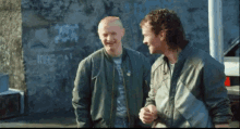 two men are standing next to each other in front of a wall with graffiti on it that says " imbecil "