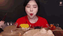 a woman in a red shirt is sitting at a table with bowls of food on it
