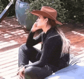 a woman wearing a brown cowboy hat is sitting on a wooden deck .