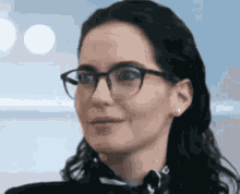 a woman wearing glasses and a black shirt is smiling .