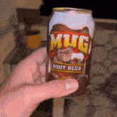 a person holds a can of mug root beer in their hand