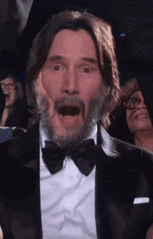 a man with a beard wearing a tuxedo and bow tie is making a funny face .