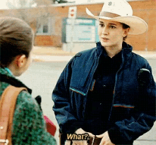 a woman wearing a cowboy hat is talking to another woman with a sign that says what