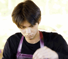 a man wearing a black shirt and a purple apron is looking down