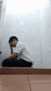 a man in a white shirt is kneeling down in a bathroom with his hands on his face