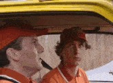 two men in red hats are sitting in a yellow car