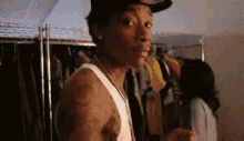 a man wearing a hat and a white tank top is standing in front of a closet .