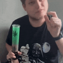 a man wearing a darth vader t-shirt is holding a green bong