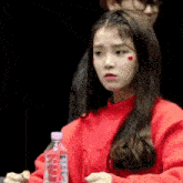 a woman in a red sweater is holding a bottle of water and making a funny face .