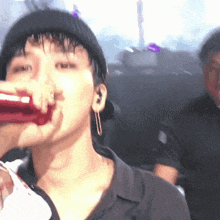 a man is drinking from a red bottle while wearing a hat and earrings .