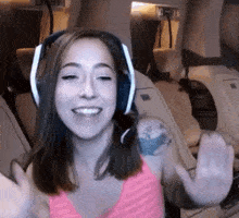 a woman wearing headphones and a pink tank top is waving