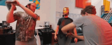 a man wearing an iron man mask is drinking from a bottle while two other men laugh .