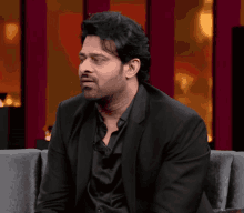a man in a black suit and black shirt sits on a couch