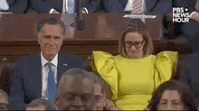 a woman in a yellow dress is sitting next to a man in a suit and tie in a parliament .