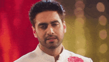 a man with a beard and a white shirt is standing in front of a red curtain and looking at the camera .
