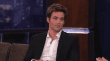 a man in a suit and white shirt is sitting on a couch talking to a woman .