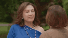 a woman in a blue shirt is being touched by another woman 's hand .