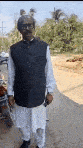 a man wearing a black vest and white pants is standing on a street .