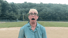 a man wearing glasses and a hat is making a funny face in front of a baseball field