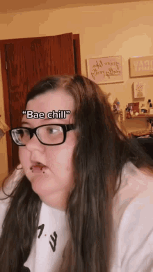 a woman wearing glasses and a white shirt says " bae chill " on her face