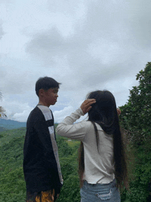 a boy and a girl standing next to each other with trees in the background