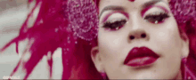 a close up of a woman 's face with red lipstick and pink hair .