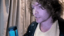 a man with curly hair is singing into a microphone in front of a window .