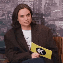 a woman in a brown jacket is holding a yellow sign with a k on it