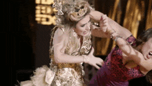 a woman in a gold dress is fighting another woman in a red dress