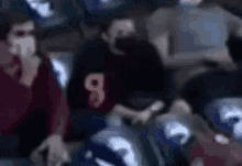 a blurry picture of a group of people sitting in a stadium wearing masks .