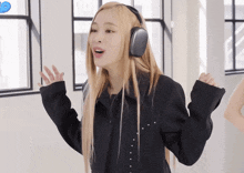 a woman with long blonde hair wearing headphones stands in front of a window